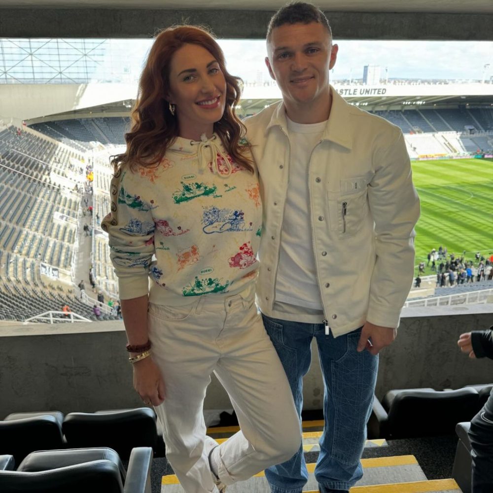 Charlotte und Kieran Trippier lächeln in die Kamera, im Hintergrund ist der leere St. James' Park zu sehen.