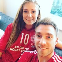 Fußball-Profi Christian Eriksen und seine Ehefrau Sabrina Kvist Jensen tragen das Dänemarktrikot und lächeln in die Kamera.